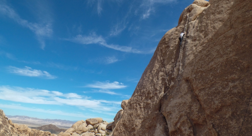 A rock climber is near the top of a rock wall with blue skies above